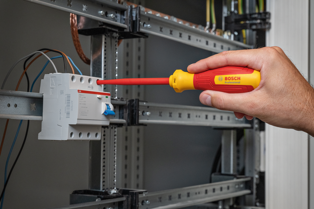 Oseba uporablja izoliran izvijač za prilagajanje ožičenja v električni plošči.